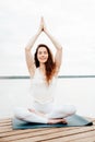 Beautiful young woman in white sports clothes is sitting on  wooden pier on lake in  lotus position with namaste gesture Royalty Free Stock Photo