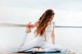 Beautiful young woman in white sports clothes is sitting on  wooden pier on lake in  lotus position with namaste gesture Royalty Free Stock Photo