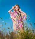 Beautiful young woman in wild flowers field on blue sky background. Portrait of attractive red hair girl with long hair relaxing Royalty Free Stock Photo