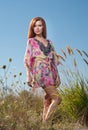 Beautiful young woman in wild flowers field on blue sky background. Portrait of attractive red hair girl with long hair relaxing Royalty Free Stock Photo