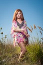 Beautiful young woman in wild flowers field on blue sky background. Portrait of attractive red hair girl with long hair relaxing Royalty Free Stock Photo