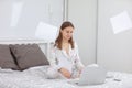 Beautiful Young Woman Working from Home - Female Entrepreneur Sitting on Bed with Laptop Computer, blank sheets of papers are Royalty Free Stock Photo
