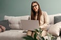 Beautiful young woman working with laptop on couch. Businesswoman using laptop managing her business. Home office during Coronavir