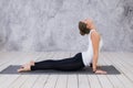 Beautiful young woman working out indoors, doing yoga exercise in the room with white walls, downward facing dog pose