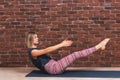 Beautiful young woman working out in loft interior on brick wall background with copy space, doing abdominal exercises and holding Royalty Free Stock Photo