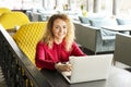 Beautiful young woman working remotely on her fashionable laptop at hipster coffee shop. Happy female freelancer with trendy wrist Royalty Free Stock Photo