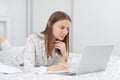 Beautiful young woman working, using laptop computer and makes notes in the bedroom at home. Freelancer. Writing, typing. Girl Royalty Free Stock Photo