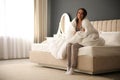 Beautiful young woman wrapped with soft blanket sitting on bed at home Royalty Free Stock Photo