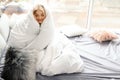 Beautiful young woman wrapped in soft blanket sitting near window at home Royalty Free Stock Photo