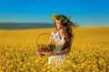 Beautiful young woman with wreath on long healthy hair over Yellow rape field landscape background. Attracive brunette girl with