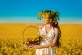 Beautiful young woman with wreath on long healthy hair over Yellow rape field landscape background. Attracive brunette girl with