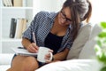 Beautiful young woman writting on the notebook while drinking coffee.