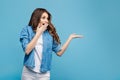 Beautiful young woman in yellow sweater posing on blue background. Attractive woman pointing fingers to the right with Royalty Free Stock Photo