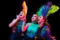 Beautiful young women in carnival and masquerade costume in colorful neon lights on black background