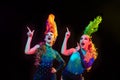 Beautiful young women in carnival and masquerade costume in colorful neon lights on black background