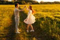 Beautiful young woman in dress dancing with loving boyfriend on green meadow in summer evening during sunset with soft Royalty Free Stock Photo