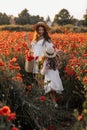 Beautiful young woman with girl in field with poppies, mother and daughter in white dresses and straw hats in evening at sunset,