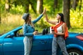 Beautiful young women giving high five, having fun together, cheering with raised arms driving modern convertible car on summer