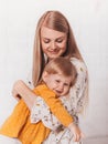 A beautiful young woman holds her pretty daughter Todler in her arms on a bright background. Vertical portrait