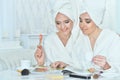 Beautiful young women sitting at table with magazine and applying makeup Royalty Free Stock Photo