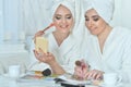 Beautiful young women sitting at table with magazine and applying makeup Royalty Free Stock Photo