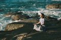 A beautiful young yoga woman meditates in the lotus position, sitting on the rocks on the ocean shore. Royalty Free Stock Photo