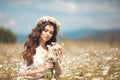 Beautiful young girl with flowers enjoying in chamomile field. Carefree happy brunette woman with chaplet on healthy wavy hair