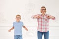 A beautifull mother in a plaid shirt and her little son in a blue shirt do exercises and warm up. Boy waving his hands