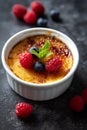 A beautifully crafted creme brulee adorned with a few berries as decoration. ItÃ¢â¬â¢s presented in a white ramekin on a dark,