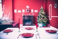 Beautifully laid new year table with red plates and Cutlery on a background of decorated room with Christmas tree Royalty Free Stock Photo