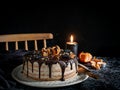 Beautifully styled and decorated birthday cake with one candle lit up, on a table with chair in the background,oranges, walnut and