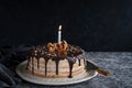 Beautifully styled and decorated birthday cake with one candle lit up, on a table, oranges, walnut and chocolate decoration, dark