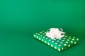 A beautifully wrapped gift with a white bow lies on a green background. The gift box is packed in green paper with white peas. Royalty Free Stock Photo