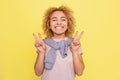 Beautifyl girl is smiling and showing a piece symbol with fingers on her hands. Isolated on yellow background.