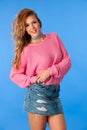 Beautuful blond woman in pink sweater and jeans skirt dance and pose over vibrant blue background Royalty Free Stock Photo