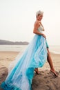 Beautuful blonde short haired woman posing in blue tulle long train dress on black sandy beach Royalty Free Stock Photo