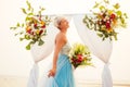 Beautuful blonde short haired woman posing in blue tulle long train dress near wedding flower arch with tropical bouquet Royalty Free Stock Photo