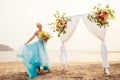 Beautuful blonde short haired woman posing in blue tulle long train dress near wedding flower arch with tropical bouquet Royalty Free Stock Photo