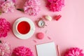 Beautuful flat lay with notepad, pencil, alarm clock, peony flowers, a cup of tea and macarons on a light pink