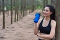 Beauty Asian sport woman resting and holding drinking water bottle and relaxing in middle of forest after tired from jogging.