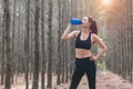 Beauty Asian sport woman resting and holding drinking water bottle and relaxing in middle of forest after tired from jogging. Girl