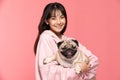 Beauty Asian young woman holding dog pug breed on her arm smile and happiness,Owner hug her cute pet dog with love on pink Royalty Free Stock Photo