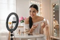Beauty blogger with makeup product recording video in room at home. Using ring lamp and smartphone