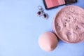 Beauty box, loose matte mineral powder and blush with a beauty blender for makeup and silver earrings on a blue background. Royalty Free Stock Photo