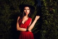 Beauty brunette women in red dress & hat pose at night park. Royalty Free Stock Photo