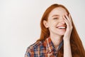 Beauty. Close-up of happy young woman with red natural hair and pale skin, smiling joyfully and covering half of face