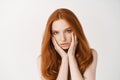 Beauty. Close-up of natural young woman with ginger hair, touching pale clean no make-up face and looking at camera Royalty Free Stock Photo