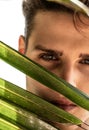 Beauty closeup portrait of handsome young man looking at the camera through green palms leaf. Summer vibes. Male model Royalty Free Stock Photo