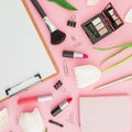 Beauty composition with clipboard, tulips, cosmetics and accessory on pink background. Top view. Flat lay. Home feminine desk.