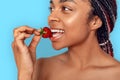 Beauty Concept. Young african woman isolated on blue biting strawberry playful side view close-up Royalty Free Stock Photo